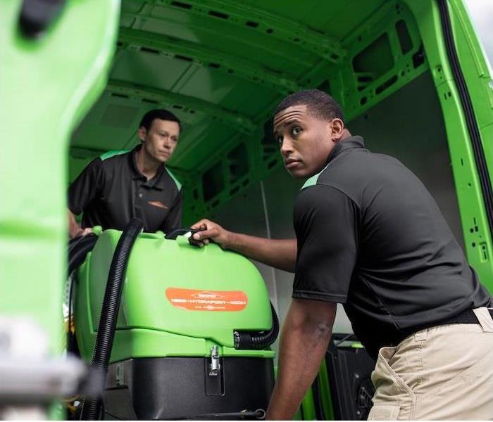  "two SERVPRO employees unloading cleaning equipment out of a green van" 